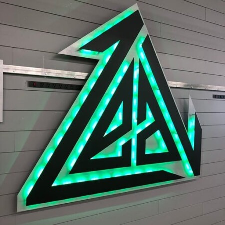 Crossfit Zeal angular mountain logo sign in black and brushed steel, halo-lit LED and glowing green.