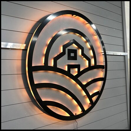 Pono Acres sign angled on the wall, the concentric cut arcs catching the warm halo.