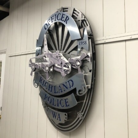 Richland Police badge sign in layered steel with patrol car and aircraft detail above a name banner.