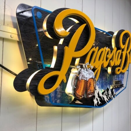 Pagosa Bar vinyl sign from the side, gold script standing off a printed mountain scene with beer steins.