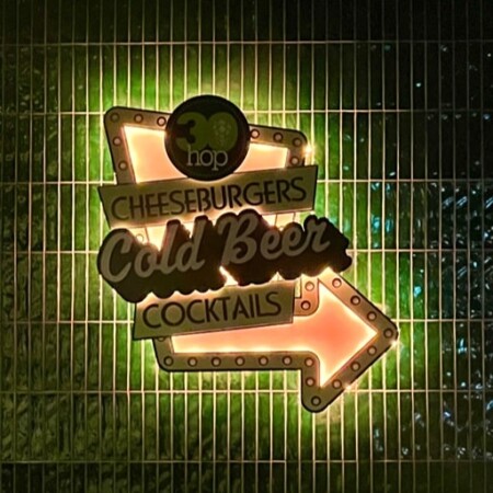 30 Hop bar sign lit warm amber and green against a dark metal grille wall.