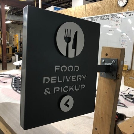 The Food Delivery & Pickup lightbox and blade sign clamped to a post in the shop before install.