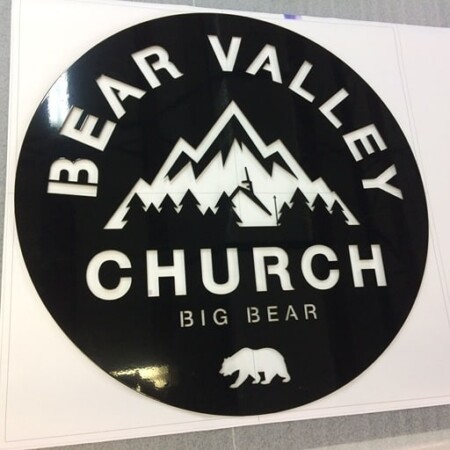Bear Valley Church round sign in black and white with a mountain range and a bear silhouette, mounted on a template.