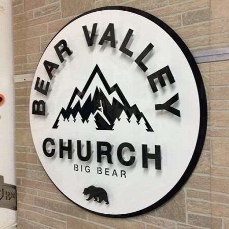 Bear Valley Church round sign in black and white with a mountain range and a bear silhouette, mounted on brick.