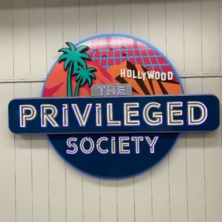 The Privileged Society round sign, a Hollywood sunset and palms above the name on a navy band.