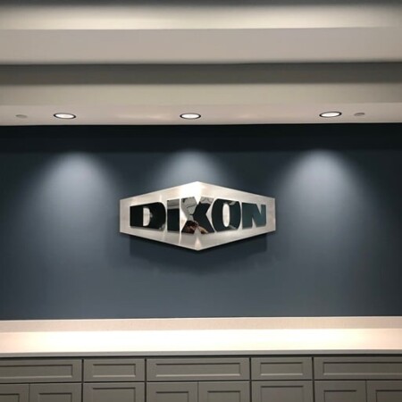 Dixon hexagonal lobby sign in polished aluminum with cut-out lettering, under ceiling downlights.