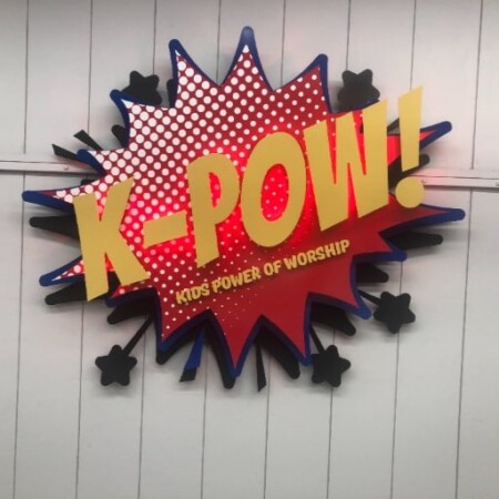 K-POW! Kids Power of Worship sign shaped as a comic-book starburst in red halftone and gold.