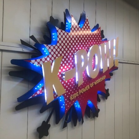 K-POW! vinyl sign with blue LEDs firing behind the starburst, the gold letters catching the light.