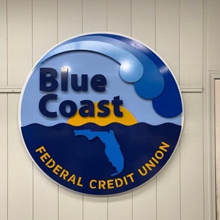 Blue Coast Federal Credit Union round sign with a layered wave above the Florida coastline in yellow.