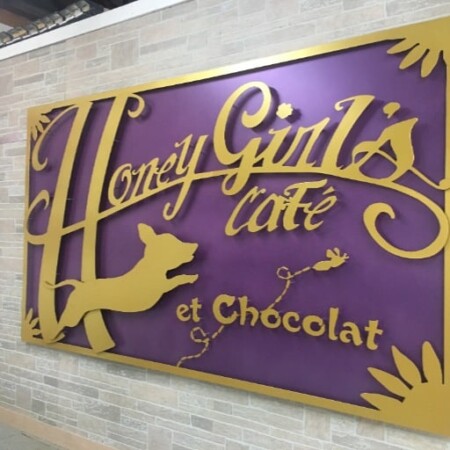 Honey Girl's Café et Chocolat sign in purple with gold script and a leaping fox, mounted on brick.