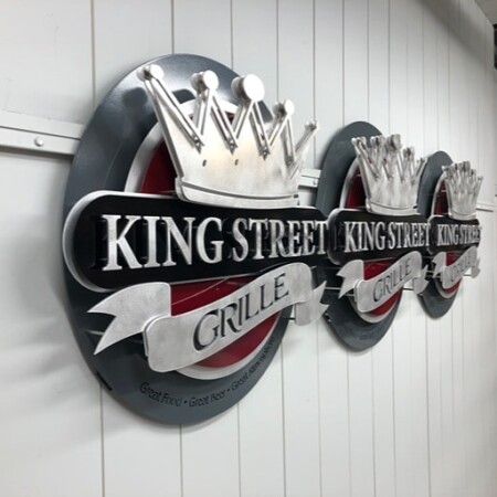 King Street Grille oval signs with silver crowns above ribbon lettering, three finished and lined up.