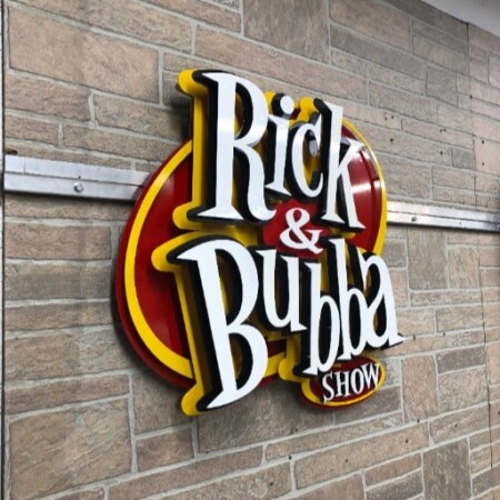 The Rick & Bubba Show sign with white script over red and yellow layers, mounted on brick.