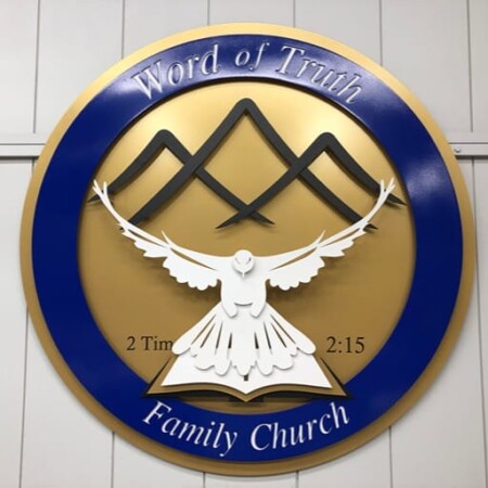 Word of Truth Family Church round sign, a white dove over an open book inside a blue and gold ring.