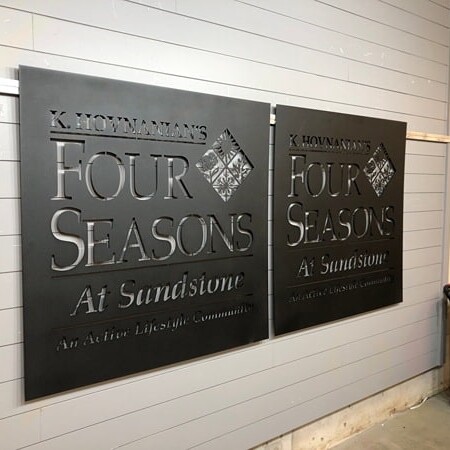 Two K. Hovnanian's Four Seasons at Sandstone panels finished in the shop, pale lettering on dark metal.