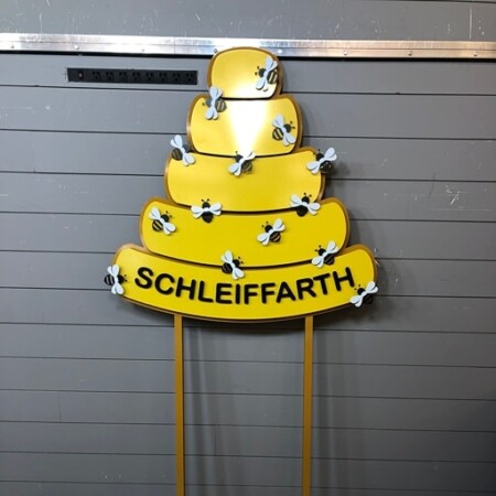 Schleiffarth home sign shaped as a yellow beehive with bees across it, post-mounted with the name on a banner.