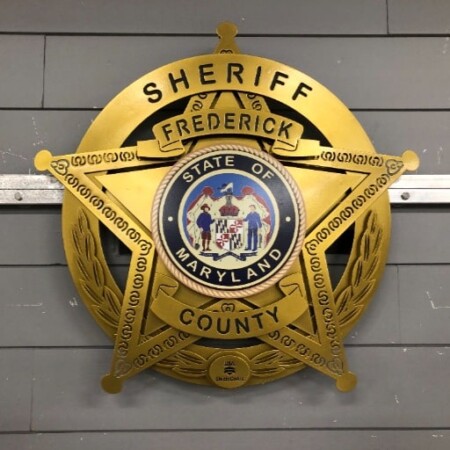 Frederick County Sheriff star badge in gold with the Maryland state seal at its center, on a wreath.