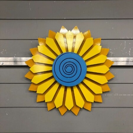Sunflower wall piece with layered yellow petals around a blue spiral center.
