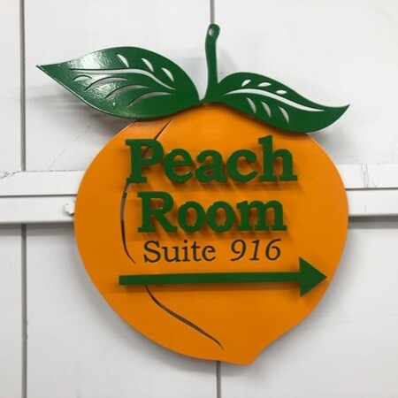 Peach Room Suite 916 wayfinding sign cut in the shape of a peach, green lettering and a direction arrow.