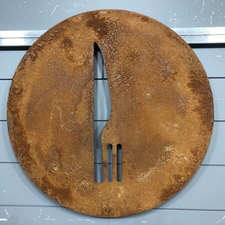 Stecca Taverna round sign in rusted steel, a knife and fork cut clean through the plate.
