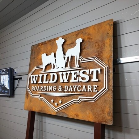 Wild West Boarding & Daycare sign on rusted steel, three dogs in silhouette above the name, post-mounted.