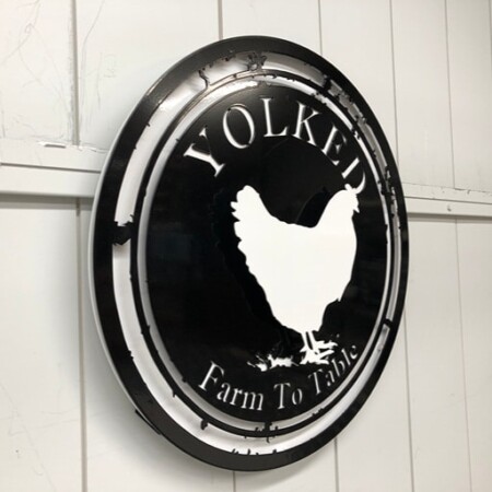 Yolked Farm To Table sign angled on the wall, the raw steel ring standing proud of the black face.