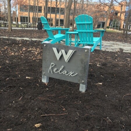 Relax marker in mottled steel standing beside a pair of teal Adirondack chairs in the courtyard.