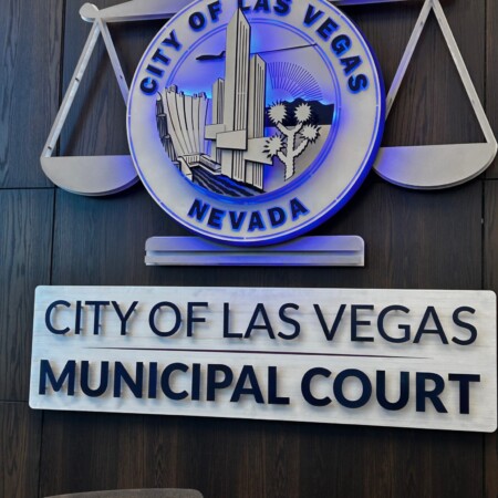 City of Las Vegas Municipal Court seal with scales of justice above a dimensional name plaque, on wood panelling.
