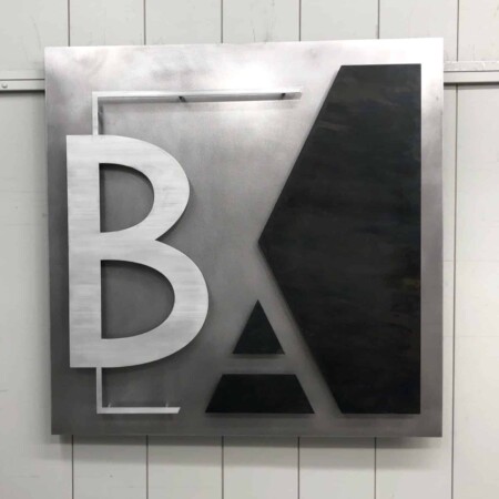 BA Blumentals Architecture monogram sign in brushed aluminum and black, the letters cut as interlocking shapes.