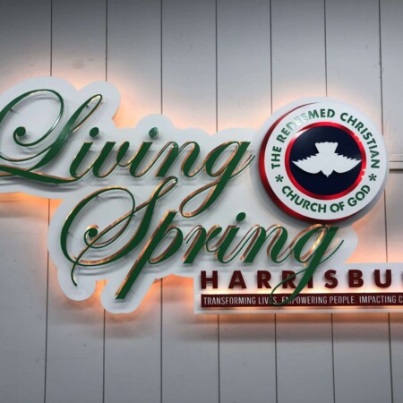 Living Spring Harrisburg sign with green script over a red name bar and a church roundel, glowing warm.