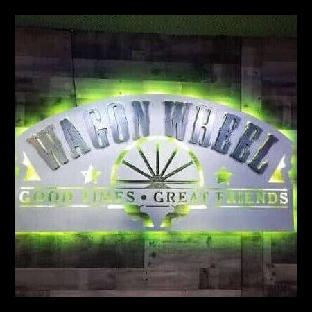 Wagon Wheel sign close up, the green LED halo flaring around the brushed arch and its cut spokes.