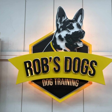 Rob's Dogs Dog Training sign with a German shepherd above a yellow banner on a black shield.